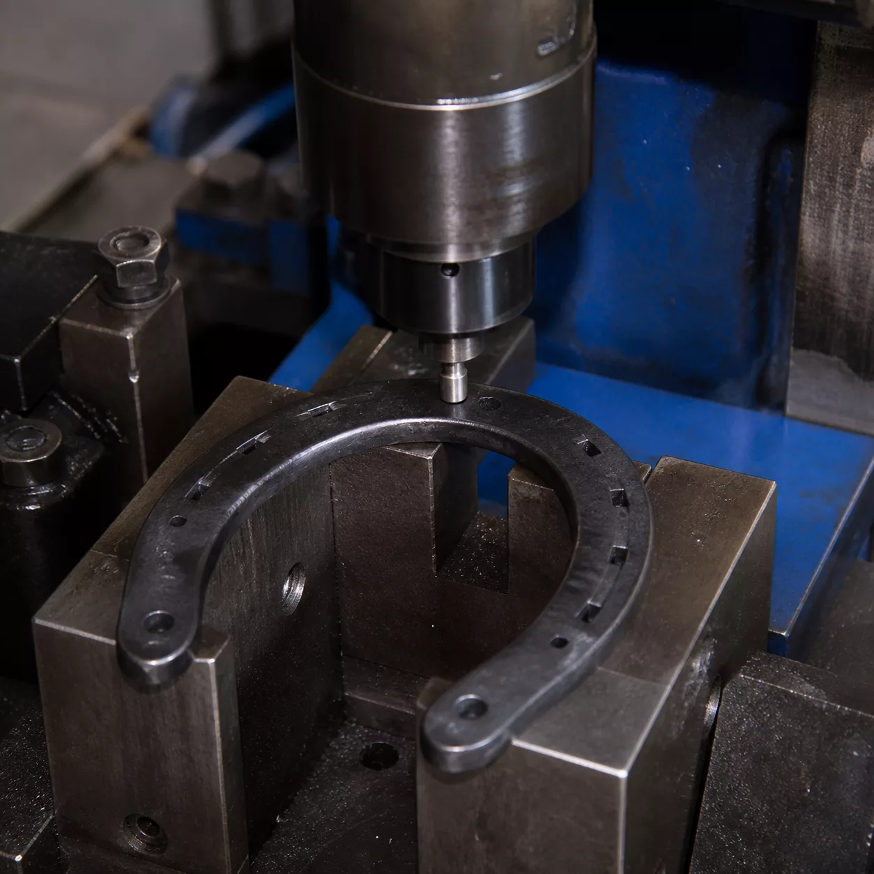 Precision nail-hole punching on an open U-shaped horseshoe