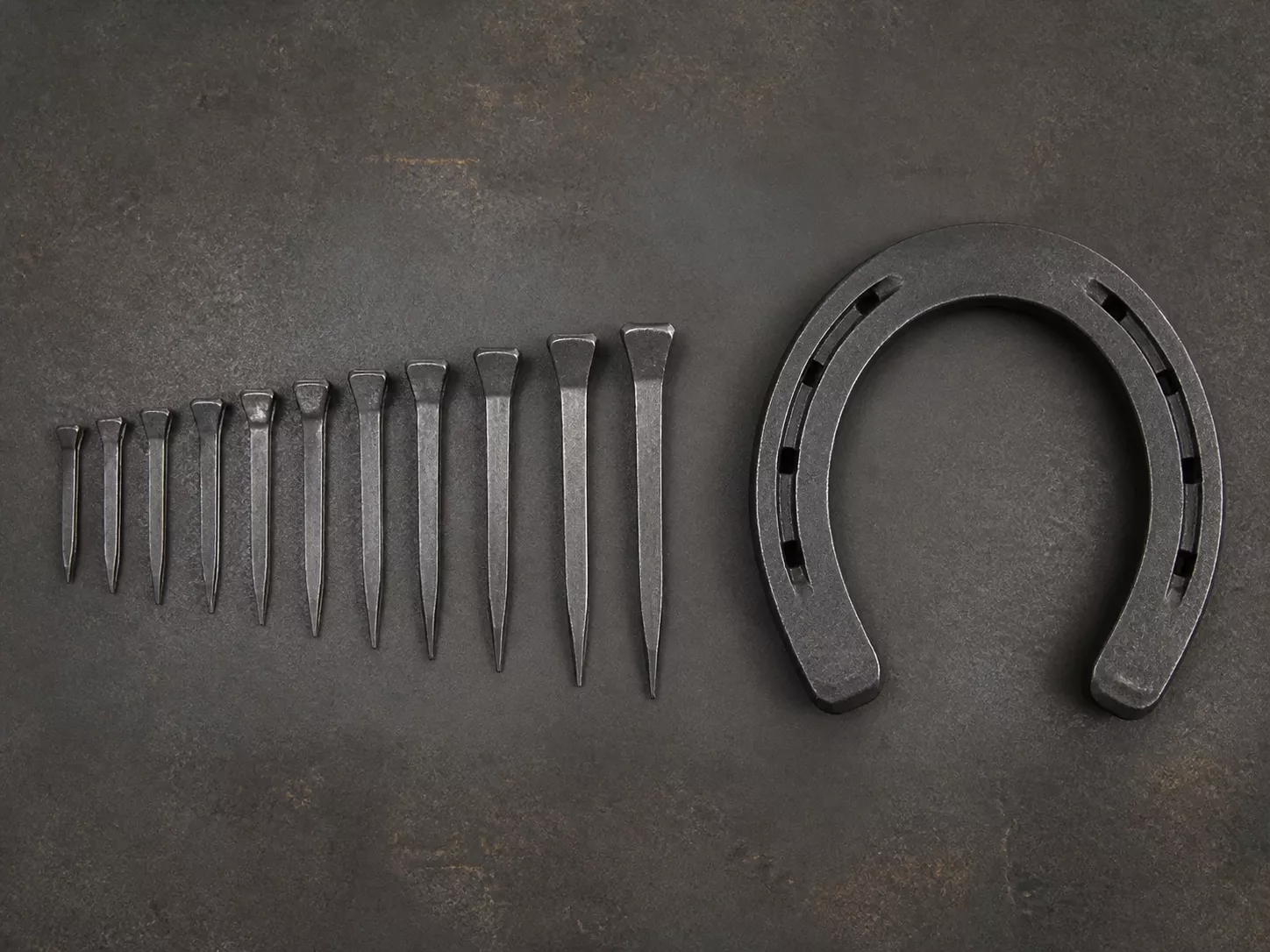 Authentic forged horseshoe nails beside an open U-shaped steel horseshoe